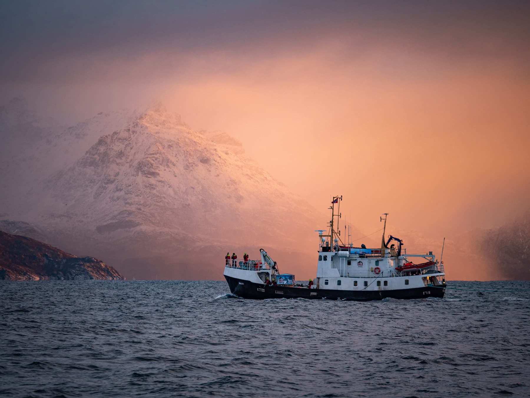 ship steaming with orange backdrop of sunlight hitting the low clouds